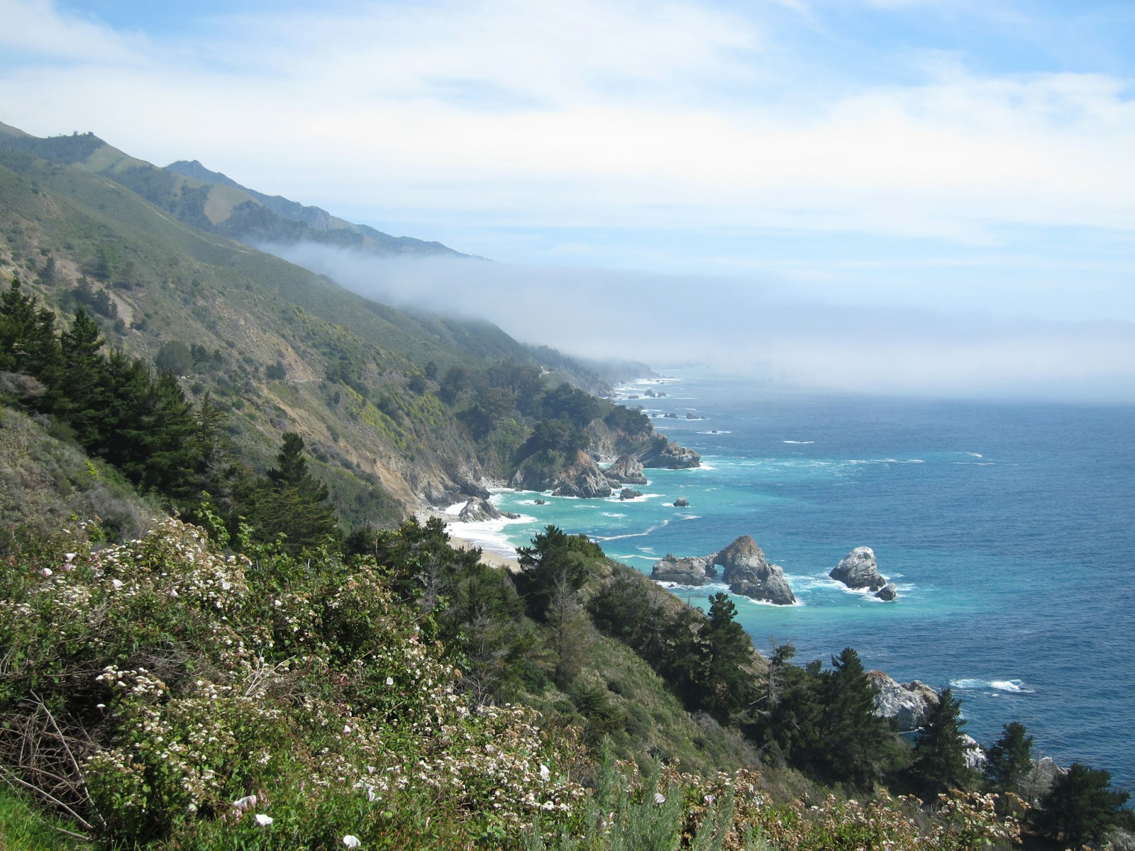 Rocky coastal cliffs meet the blue ocean beneath a soft layer of fog